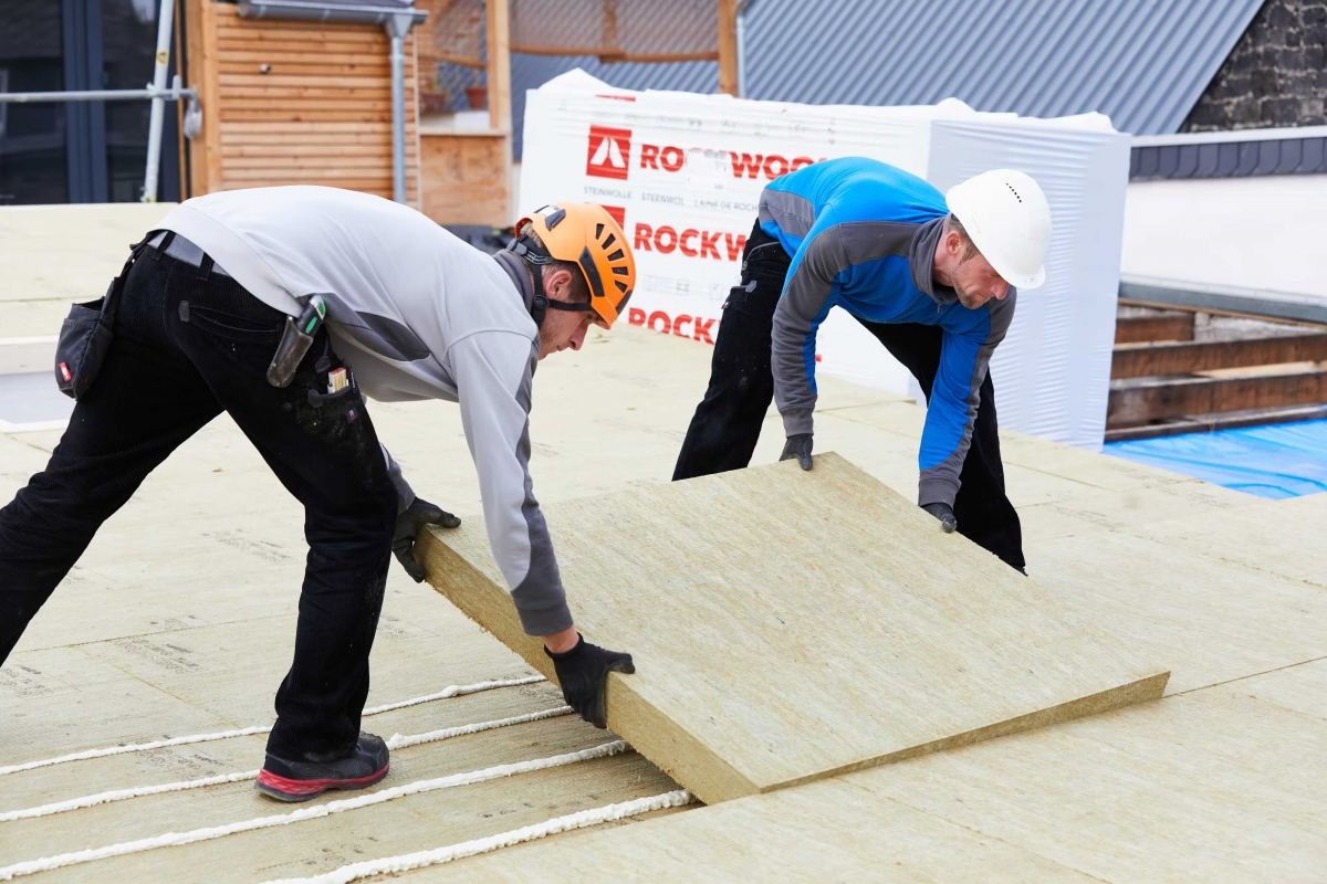 Deux professionnels installant des panneaux d'isolation Rockwool sur un toit.